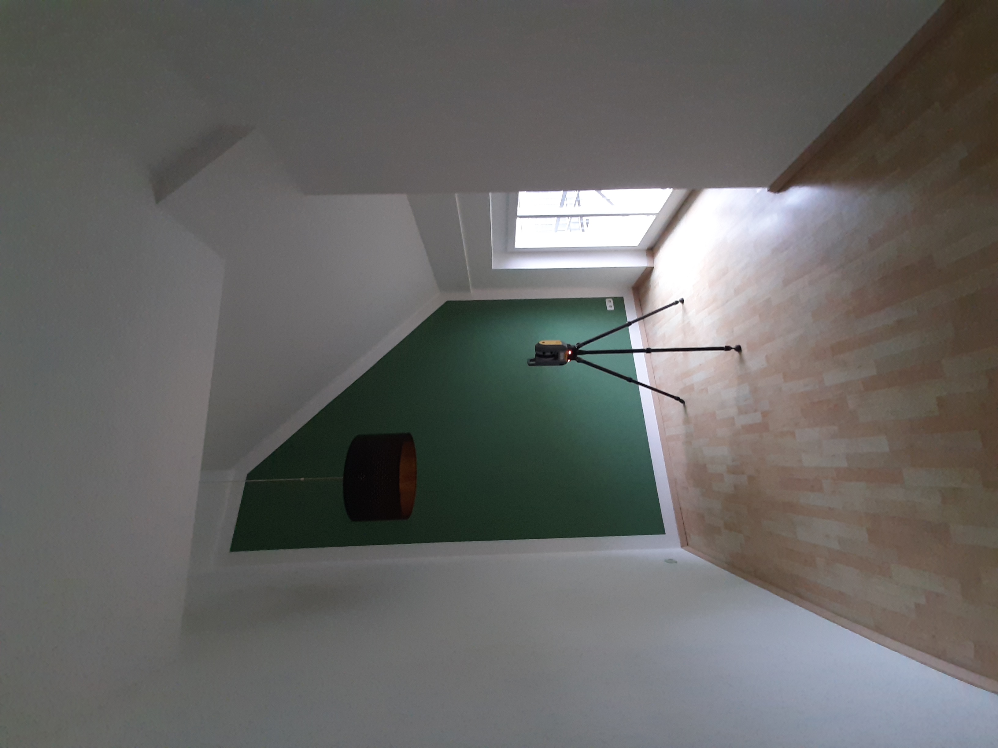 Ein leerer Raum mit hoher Decke, in dessen Mitte ein Laserscanner auf einem Stativ steht. Die Szene zeigt die Vermessungssituation, bei der eine Punktewolke erstellt wird, um den Raum digital und präzise zu erfassen.